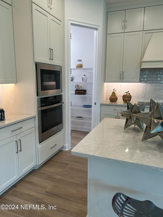 kitchen with hardwood / wood-style floors, decorative backsplash, light stone countertops, white cabinetry, and stainless steel appliances