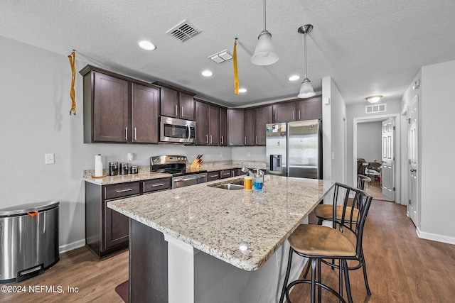 kitchen with appliances with stainless steel finishes, a breakfast bar area, a center island with sink, and dark wood-type flooring