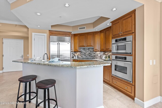 kitchen with light tile patterned floors, an island with sink, stainless steel built in refrigerator, tasteful backsplash, and ornamental molding