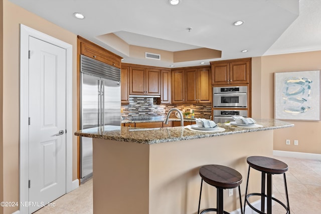 kitchen with a kitchen island with sink, a raised ceiling, backsplash, and stainless steel appliances