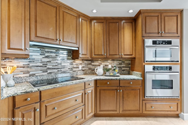 kitchen featuring stainless steel double oven, brown cabinets, black electric cooktop, and light stone countertops