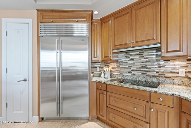 kitchen with backsplash, light stone counters, black electric cooktop, stainless steel built in refrigerator, and light tile patterned flooring