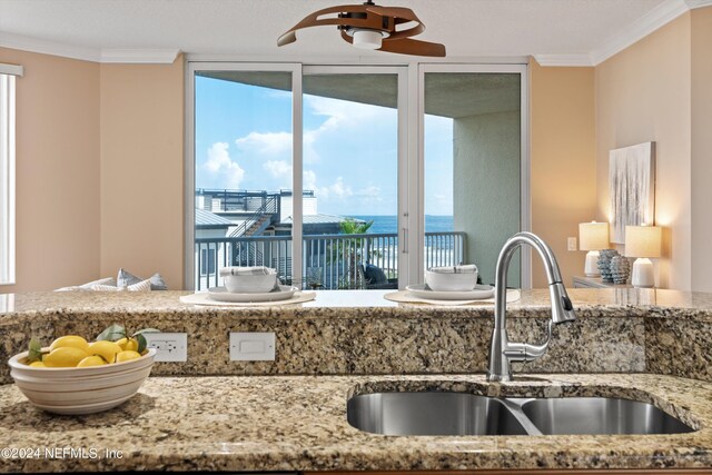 kitchen featuring a water view, a wealth of natural light, light stone counters, and sink