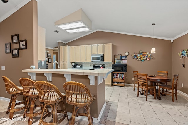 kitchen with appliances with stainless steel finishes, tile counters, vaulted ceiling, and crown molding