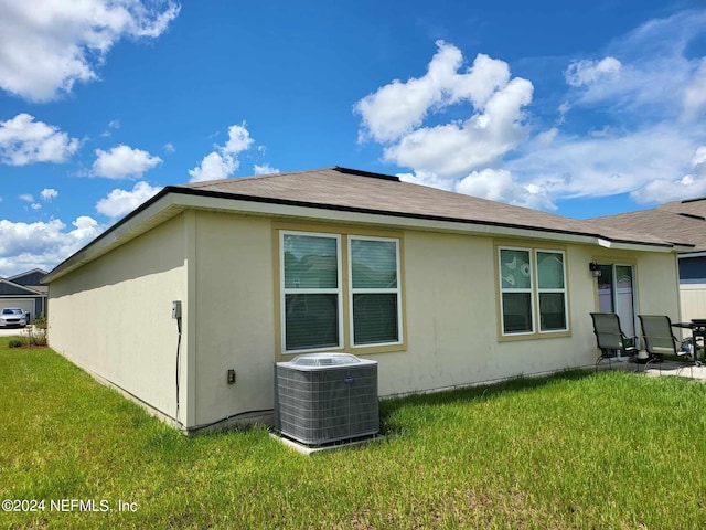 rear view of house with cooling unit, a lawn, and a patio