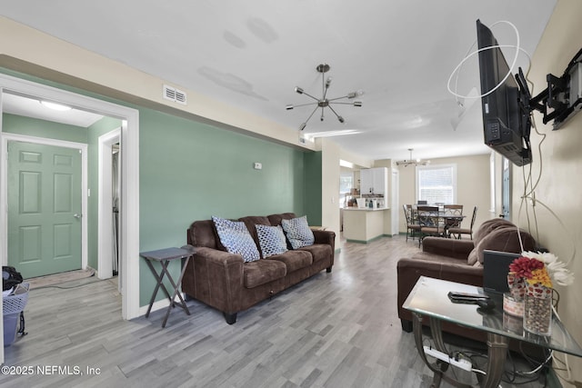 living room with baseboards, visible vents, a notable chandelier, and light wood-style floors