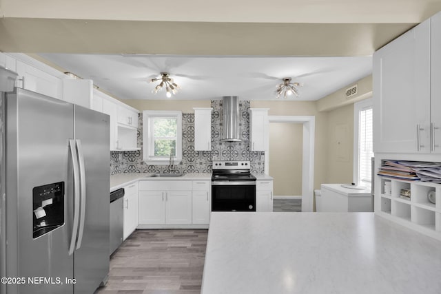 kitchen with a sink, visible vents, wall chimney range hood, light countertops, and appliances with stainless steel finishes