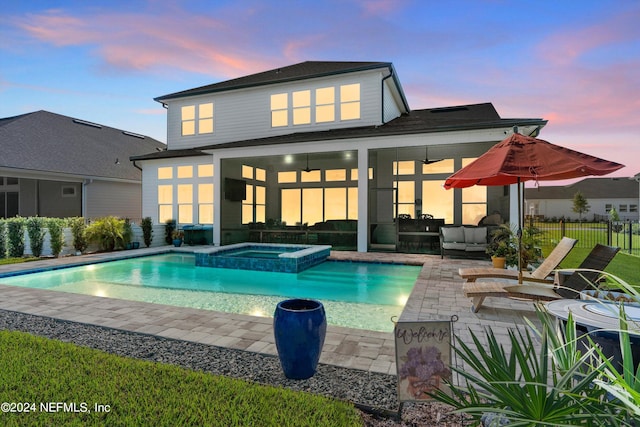 back house at dusk featuring ceiling fan, a swimming pool with hot tub, and a patio area