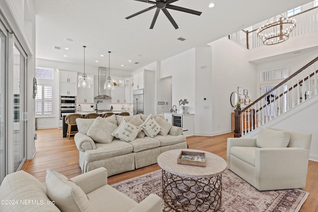 living room featuring ceiling fan with notable chandelier, beverage cooler, light wood-type flooring, and sink