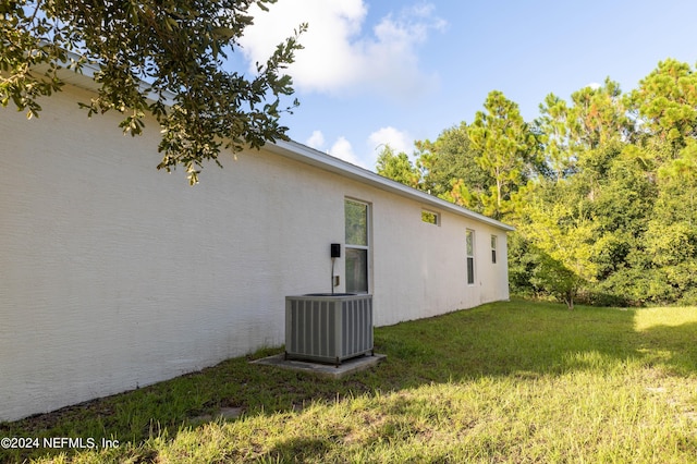 view of side of home featuring a yard, central AC, and stucco siding