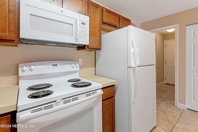 kitchen with a textured ceiling, light tile patterned floors, and white appliances