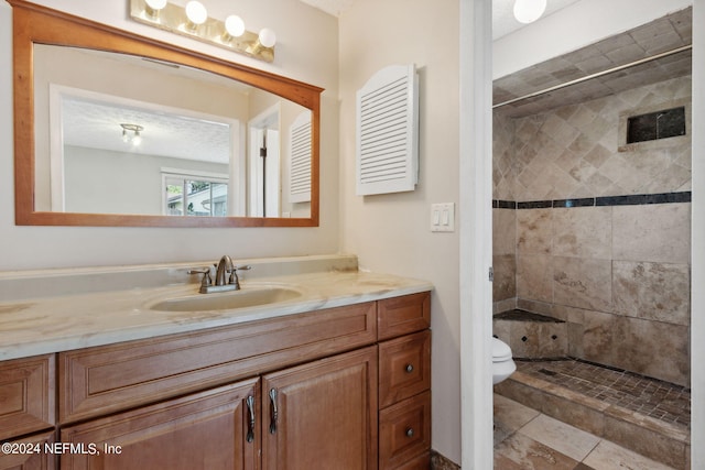 bathroom with a textured ceiling, tiled shower, vanity, and toilet