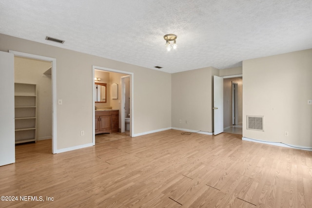 unfurnished bedroom with light hardwood / wood-style floors, a closet, a textured ceiling, a walk in closet, and ensuite bath