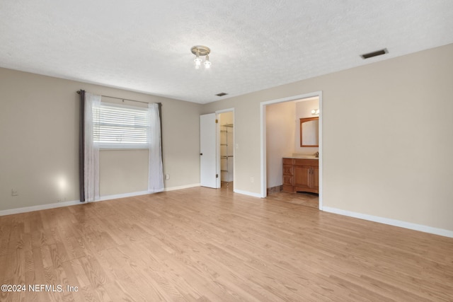 interior space with connected bathroom, a closet, light wood-type flooring, a textured ceiling, and a walk in closet