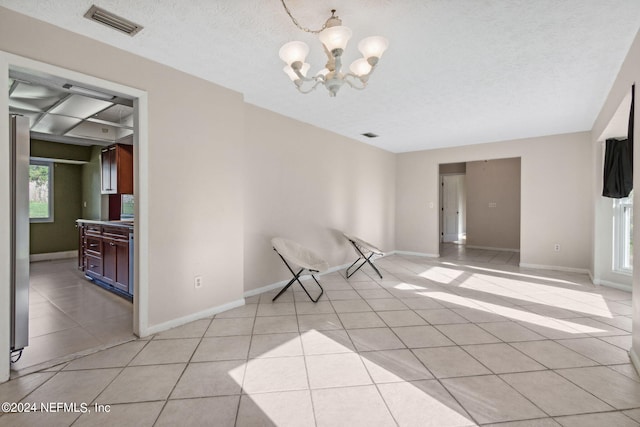 spare room featuring a textured ceiling, light tile patterned floors, and a notable chandelier