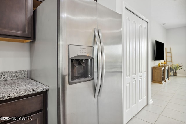 kitchen with light tile patterned floors, stainless steel fridge, dark brown cabinets, and light stone countertops