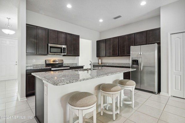 kitchen with a kitchen island with sink, light stone counters, sink, appliances with stainless steel finishes, and a breakfast bar area