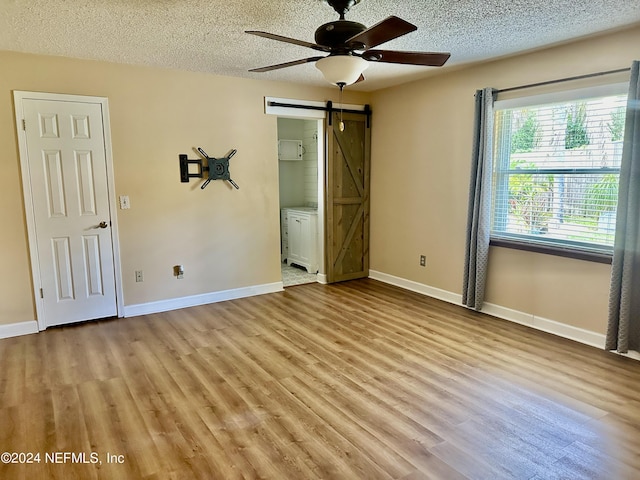 unfurnished bedroom featuring light wood-style floors, a barn door, and a textured ceiling