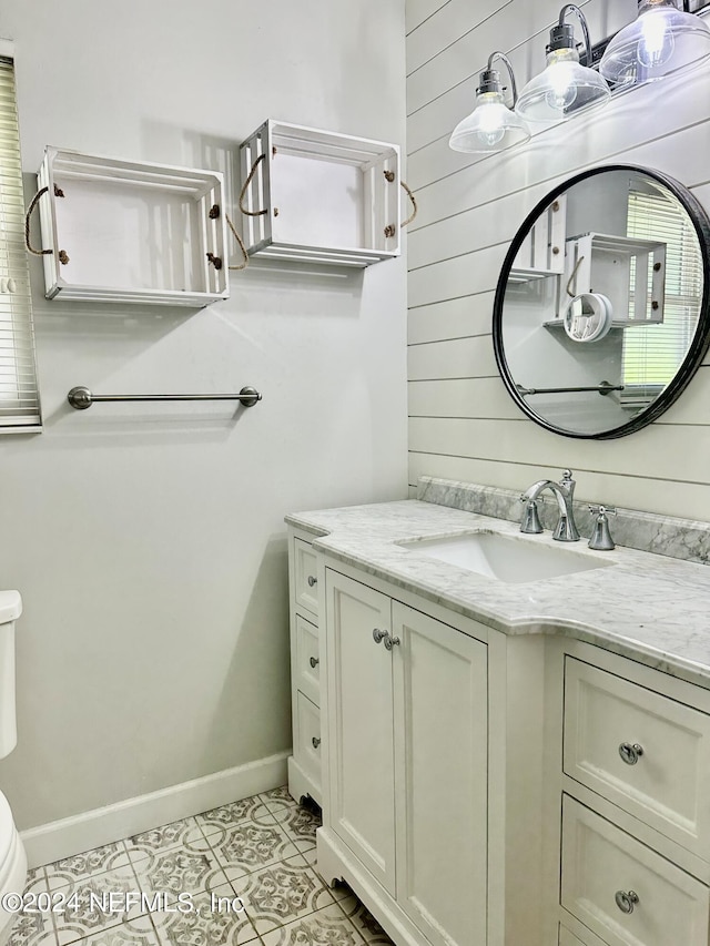 half bathroom with toilet, wooden walls, vanity, baseboards, and tile patterned floors