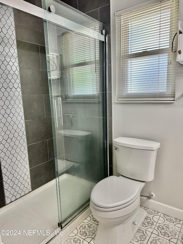 bathroom featuring toilet, tile patterned flooring, baseboards, and a shower stall