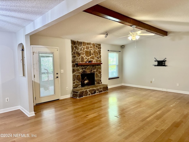 unfurnished living room with a textured ceiling, a stone fireplace, lofted ceiling with beams, and wood finished floors