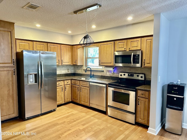 kitchen with stainless steel appliances, a sink, visible vents, light wood-style floors, and decorative backsplash