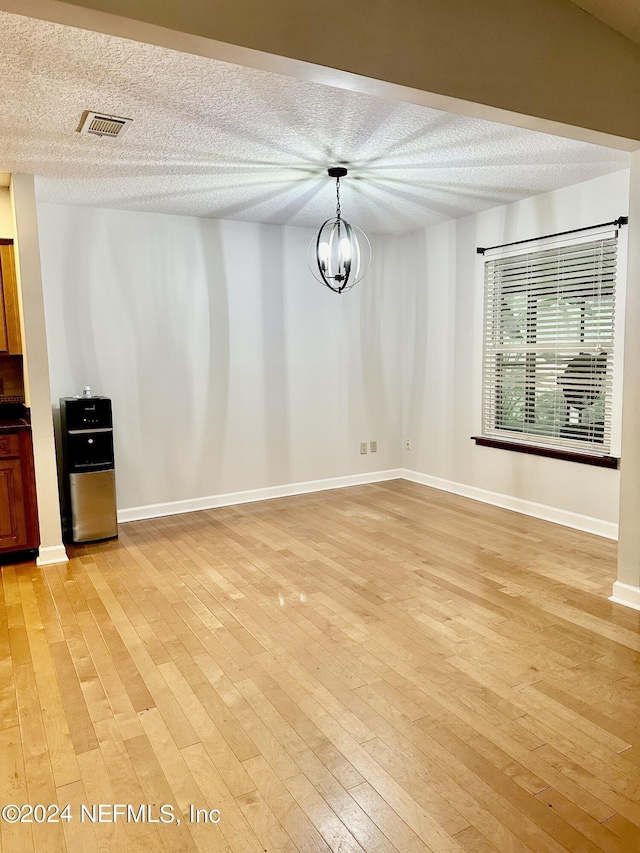 unfurnished dining area with an inviting chandelier, light wood-style flooring, visible vents, and a textured ceiling