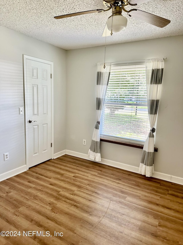 empty room with ceiling fan, a textured ceiling, wood finished floors, and baseboards