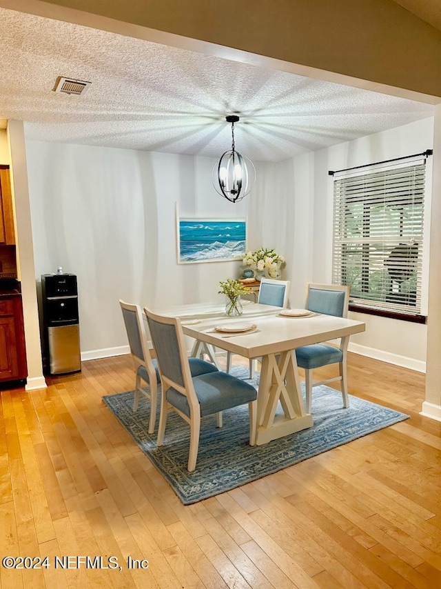 dining space with light wood-style floors, visible vents, a chandelier, and a textured ceiling