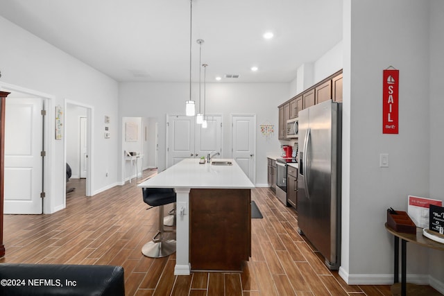 kitchen featuring stainless steel appliances, wood finish floors, a sink, and an island with sink