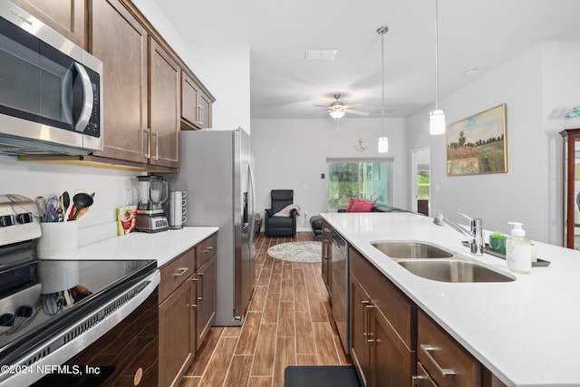 kitchen with appliances with stainless steel finishes, open floor plan, wood tiled floor, light countertops, and a sink