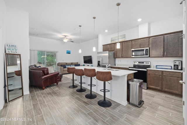 kitchen with stainless steel appliances, a breakfast bar, a sink, open floor plan, and light countertops