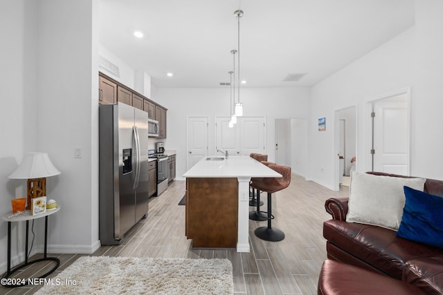 kitchen with a center island with sink, stainless steel appliances, light countertops, open floor plan, and a kitchen breakfast bar