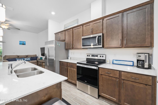 kitchen with ceiling fan, appliances with stainless steel finishes, open floor plan, light countertops, and a sink