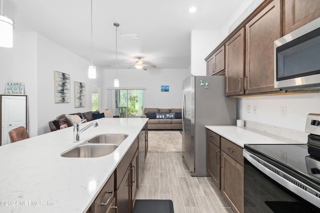 kitchen with a sink, a ceiling fan, open floor plan, appliances with stainless steel finishes, and pendant lighting