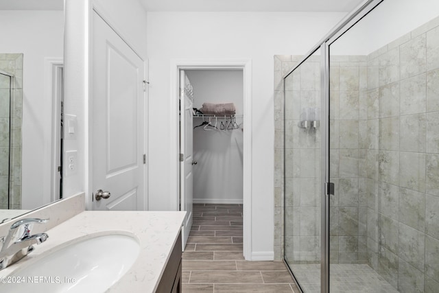 bathroom with vanity, baseboards, a spacious closet, wood tiled floor, and a stall shower