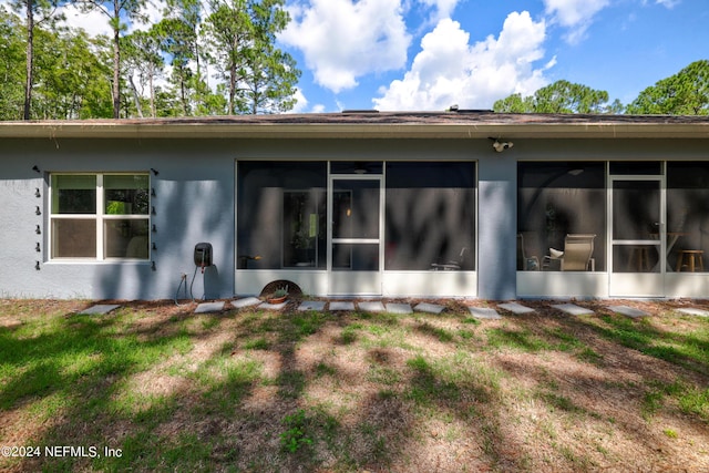 rear view of property featuring a yard, a sunroom, and stucco siding