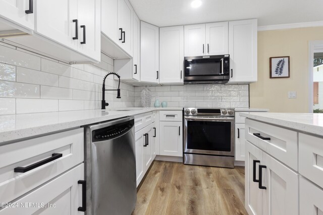 kitchen featuring stainless steel appliances, light wood-type flooring, white cabinetry, and decorative backsplash