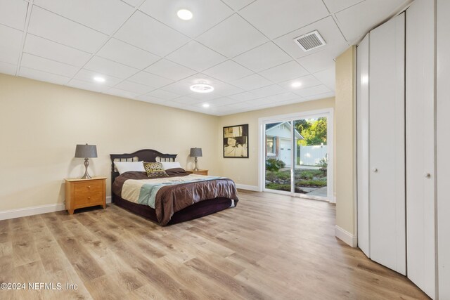 bedroom with a paneled ceiling, light hardwood / wood-style flooring, a closet, and access to outside