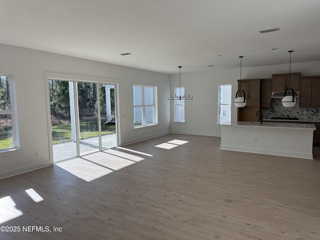 unfurnished living room with plenty of natural light, sink, an inviting chandelier, and light hardwood / wood-style floors