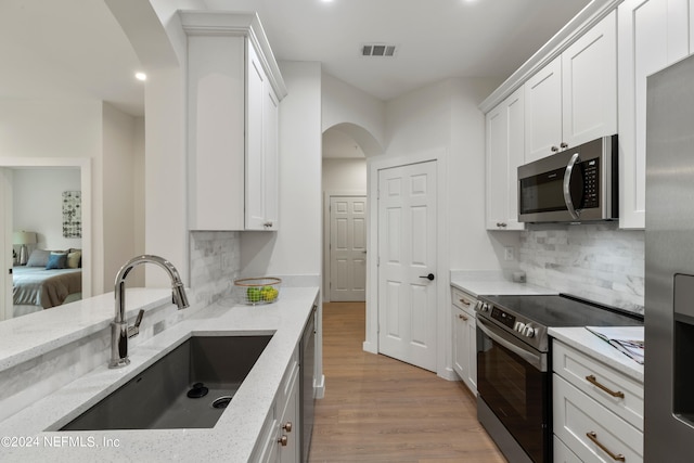 kitchen with appliances with stainless steel finishes, white cabinetry, light stone counters, light hardwood / wood-style flooring, and sink