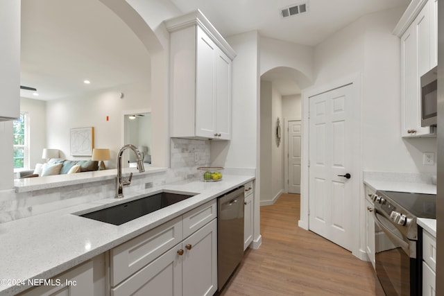 kitchen with appliances with stainless steel finishes, light wood-type flooring, sink, and white cabinets