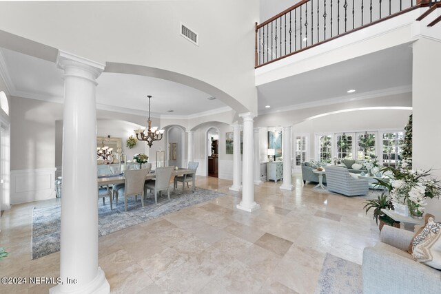 interior space featuring crown molding, a towering ceiling, an inviting chandelier, and decorative columns