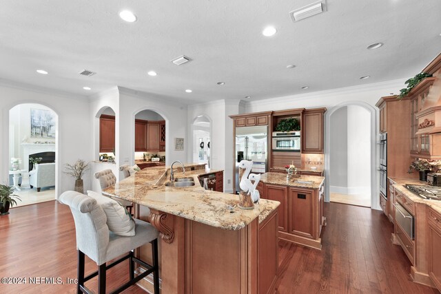 kitchen with a large island with sink, sink, dark hardwood / wood-style floors, appliances with stainless steel finishes, and a breakfast bar area