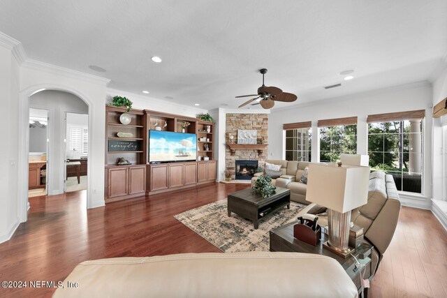 living room featuring ceiling fan, dark hardwood / wood-style flooring, crown molding, and a stone fireplace