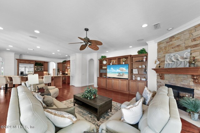 living room with ornamental molding, dark wood-type flooring, ceiling fan, and a stone fireplace