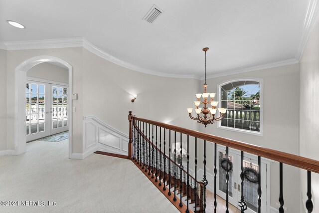 hall with ornamental molding, plenty of natural light, a notable chandelier, and carpet