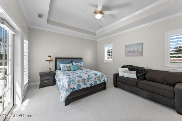 carpeted bedroom with a tray ceiling, multiple windows, crown molding, and ceiling fan