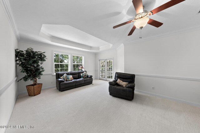 living area featuring a tray ceiling, ceiling fan, light colored carpet, and crown molding