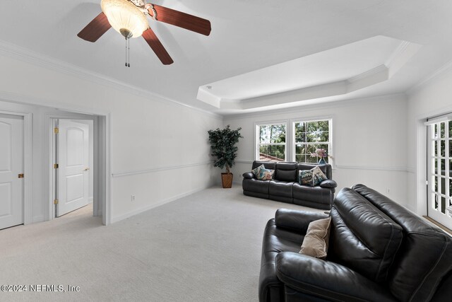 living room with a raised ceiling, ceiling fan, ornamental molding, and light colored carpet